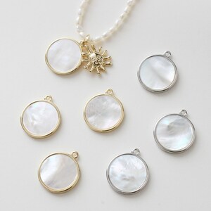 May include: Assortment of round, white mother of pearl pendants with gold and silver trim. Some pendants have a loop for hanging, while others have a sun charm attached.