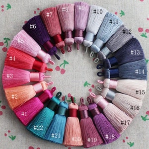 Peut inclure: Une collection de 22 pompons en soie de couleurs différentes, disposés en cercle. Les pompons sont numérotés de 1 à 22, et chaque pompon est d'une couleur différente.