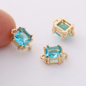 May include: Three gold-tone square-shaped charms with a blue crystal in the center. Each charm has a loop on the top and bottom for attaching to jewelry.