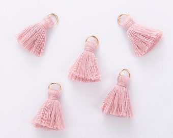 May include: Five pink tassel charms with gold jump rings. The tassels are made of soft, fluffy yarn and are perfect for adding a touch of whimsy to any project.