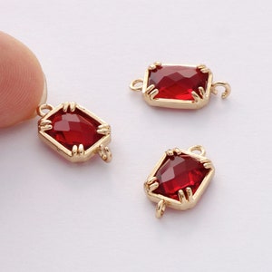 May include: Three gold-toned metal charms with red faceted glass stones. Each charm has a loop on either side for attaching to jewellery.
