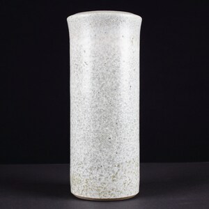 Könnte beinhalten: Eine weiße Keramikvase mit einem gesprenkelten Überzug. Die Vase ist zylindrisch geformt und hat einen glatten, abgerundeten Rand.