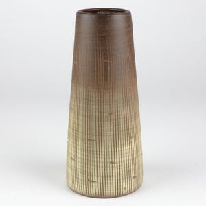 Può includere: Un vaso alto in ceramica marrone e beige con un motivo a righe verticali strutturato. Il vaso ha una base ampia che si assottiglia verso l'alto fino a un'apertura più stretta. La parte superiore è marrone più scuro, che sfuma nel beige alla base.