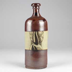 Könnte beinhalten: Eine braune Keramikflasche mit einem weißen Band, das mit einem schwarzen geometrischen Muster verziert ist. Die Flasche hat einen abgerundeten Boden und einen schmalen Hals.