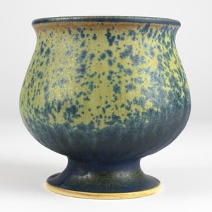 Könnte beinhalten: Eine blaue und gelbe Keramikvase mit einem gesprenkelten Überzug. Die Vase hat einen breiten, runden Körper und einen kurzen, ausgestellten Fuß.