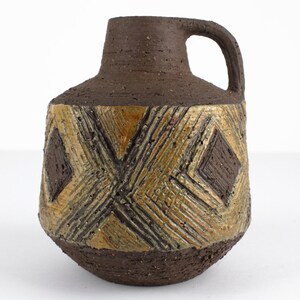Könnte beinhalten: Eine braune Keramikvase mit einem geometrischen Muster in Gold und Braun. Die Vase hat einen breiten Boden und einen schmalen Hals mit einem Henkel.