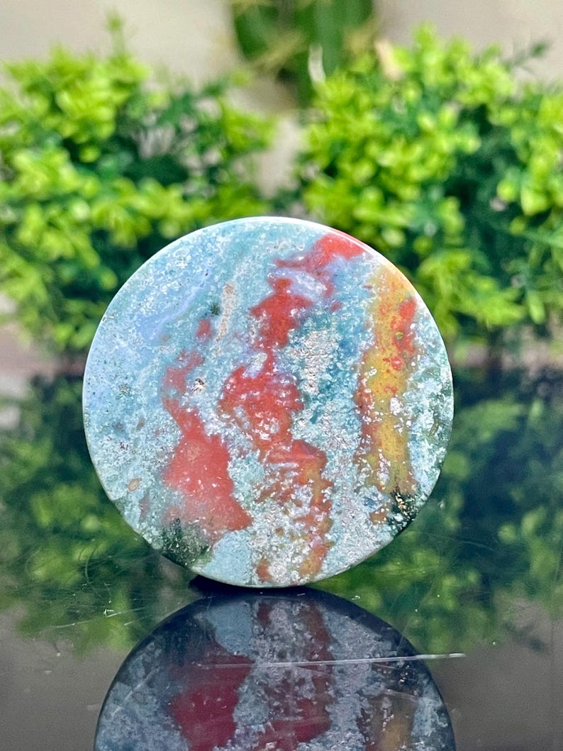 Puede incluir: Una piedra de &aacute;gata redonda, pulida, verde, roja y amarilla con un patr&oacute;n de remolino. La piedra tiene un di&aacute;metro de aproximadamente 5 cm.