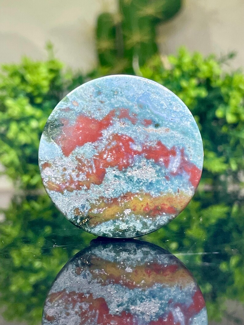 Puede incluir: Una piedra redonda y pulida con un patr&oacute;n de remolino de verde, azul, rojo y dorado. La piedra tiene un aspecto natural y org&aacute;nico.