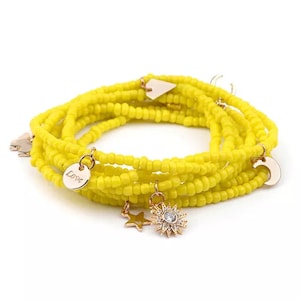 May include: A yellow beaded bracelet with multiple strands. The bracelet features gold-colored charms, including a star, a sunburst, a crescent moon, and a disc with the word "Love". The bracelet is designed to be worn as a wrap bracelet.