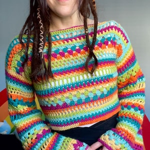 May include: A colorful, handmade crochet top with long sleeves. The top features a vibrant mix of rainbow colors, including blue, green, orange, yellow, and pink. The sleeves have a flared design. The top is a unique piece of wearable art.