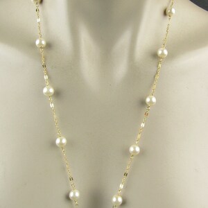 May include: A long, delicate necklace featuring creamy white pearls spaced along a thin, gold-colored chain. The necklace is displayed on a mannequin, showcasing its length and design. The pearls are round and evenly sized.