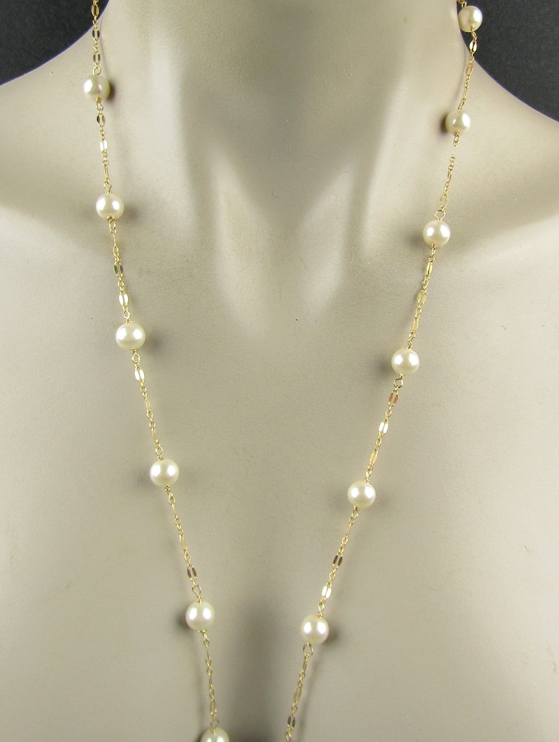 May include: A long, delicate necklace featuring creamy white pearls spaced along a thin, gold-colored chain. The necklace is displayed on a mannequin, showcasing its length and design. The pearls are round and evenly sized.