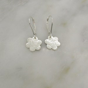 May include: A pair of silver dangle earrings with a flower-shaped charm. The flower charm has a textured design.