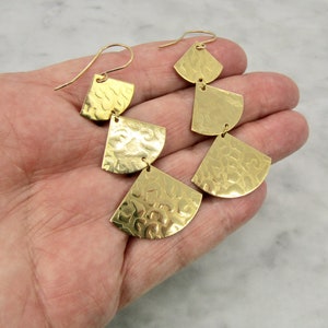 May include: Gold tone earrings with a layered design featuring three graduated, textured, crescent-shaped pieces.