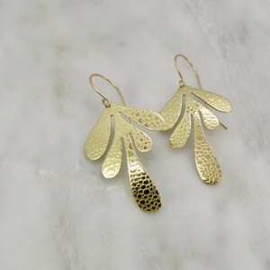 May include: A pair of gold-toned earrings with a textured, organic leaf design. The earrings are made of metal and have a hammered finish.