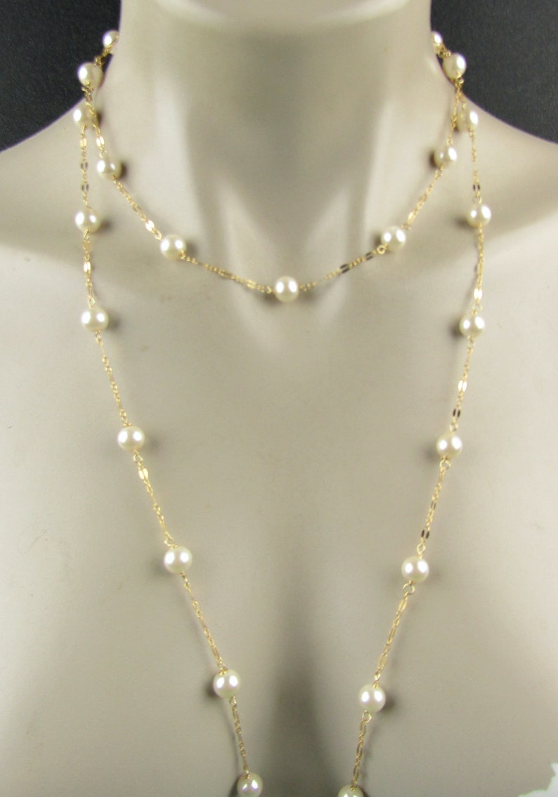 May include: A layered necklace featuring faux pearls and gold-colored chain. The necklace has two strands, one shorter and one longer, both adorned with evenly spaced, round, white pearls. The gold chain adds a touch of elegance to this classic jewelry piece.