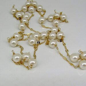 May include: A long, elegant necklace featuring large, creamy white faux pearls strung on delicate gold-colored chains. The pearls are evenly spaced, creating a classic and timeless design. The necklace is displayed against a plain white background.