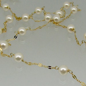 May include: A delicate necklace featuring creamy white pearls strung on a gold chain. The gold chain has small, flat, rectangular links interspersed between the pearls, creating an elegant and timeless design.