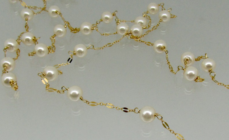 May include: A delicate necklace featuring creamy white pearls strung on a gold chain. The gold chain has small, flat, rectangular links interspersed between the pearls, creating an elegant and timeless design.