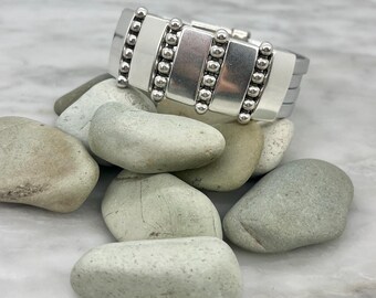 May include: Silver cuff bracelet with a beaded design. The bracelet is made of metal and has a polished finish.