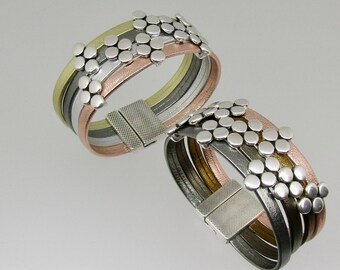 May include: Two multi-layered leather bracelets with silver and gold accents. The bracelets feature a unique design of small, round metal embellishments.