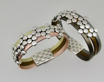 May include: Two leather bracelets with silver metal accents. The bracelets are layered and have a magnetic clasp. One bracelet is brown and the other is pink, gold, and brown.
