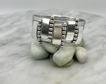 May include: Silver bracelet with a geometric design and beaded accents. The bracelet is made of metal and has a polished finish.