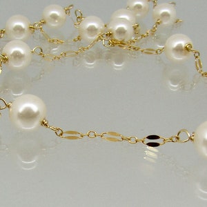 May include: A delicate necklace featuring creamy white pearls strung on a fine gold chain. The chain has a repeating pattern of small, flat gold links. The pearls are evenly spaced and vary in size.