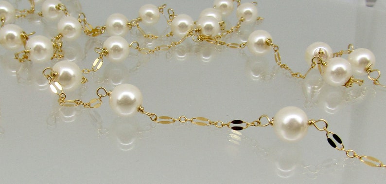 May include: A delicate necklace featuring creamy white pearls strung on a fine gold chain. The chain has a repeating pattern of small, flat gold links. The pearls are evenly spaced and vary in size.