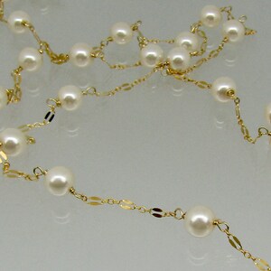 May include: A delicate necklace featuring creamy white pearls strung on a gold chain. The gold chain has small, flat, rectangular links interspersed between the pearls, creating an elegant and timeless design.