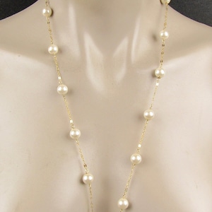 May include: A long gold chain necklace with white pearl beads. The necklace is on a white mannequin.