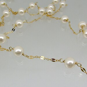 May include: A delicate necklace featuring creamy white pearls strung on a gold-colored chain. The chain has a repeating pattern of small, flat, oval links. The pearls are evenly spaced along the chain.