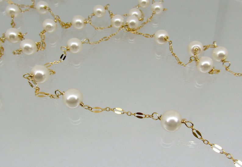 May include: A delicate necklace featuring creamy white pearls strung on a gold-colored chain. The chain has a repeating pattern of small, flat, oval links. The pearls are evenly spaced along the chain.