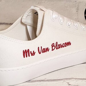 May include: White canvas sneakers with red embroidery that says "Mrs Van Blarcom". The sneakers have a white satin ribbon tied around the ankle.