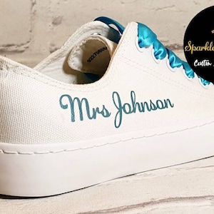 May include: White canvas shoes with a turquoise blue ribbon and the text "Mrs Johnson" embroidered in turquoise blue.
