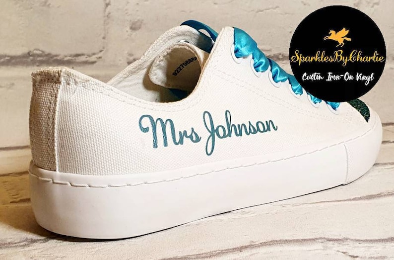May include: White canvas shoes with a turquoise blue ribbon and the text "Mrs Johnson" embroidered in turquoise blue.