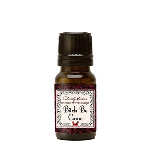May include: A small, brown glass bottle with a black cap. The label features the text "Dorothy Morrison's WICKED WITCH MOJO Bitch Be Gone" in a decorative frame with a red floral design and a small red shoe.