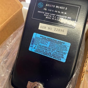 May include: A black metal lamp with a white on/off switch. The lamp has a label that reads "ARISTO M1457-3" and "PRI. 110 V. 60 Hz 36 W."