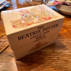 Puede incluir: Una caja blanca con una imagen de Peter Rabbit en la parte delantera. La caja está titulada "The Beatrix Potter Collection Part II, Volumes 13 to 23".