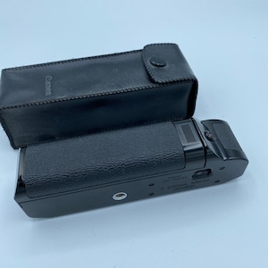 Puede incluir: Accesorio de cámara Canon Power Winder A negro con el texto "Canon Power Winder A Canon Inc. Japan" en el lateral.