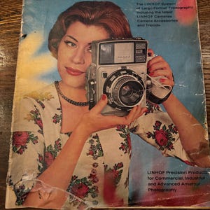 Puede incluir: Portada de catálogo de cámara "TECHNIKA" vintage con una mujer sosteniendo una cámara de gran formato. La portada tiene un fondo azul y amarillo con el texto "TECHNIKA" y la marca "LINHOF". La mujer lleva un vestido con estampado floral.
