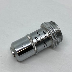 May include: A silver microscope objective lens with the text "Apo Oel 90" and "170/0.17 A115" printed on the side.