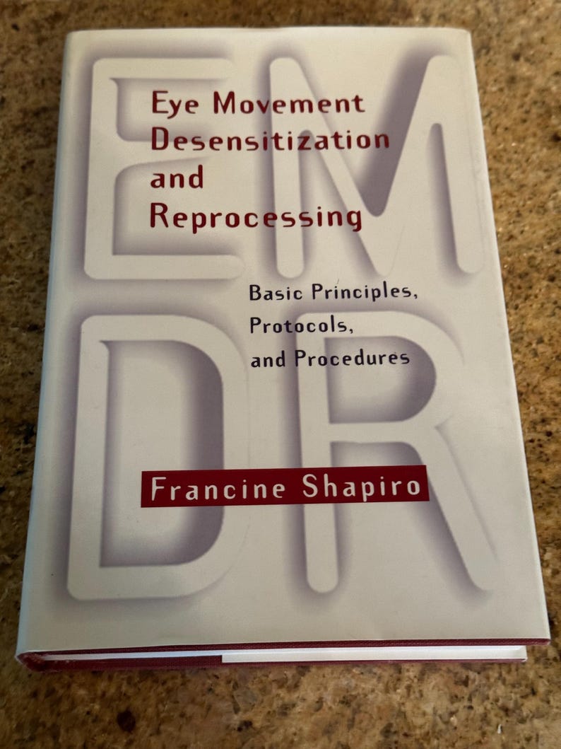 May include: A book titled "Eye Movement Desensitization and Reprocessing" by Francine Shapiro. The cover features the letters "EMDR" in large, white, shadowed font. The title is in a mix of red and black text.