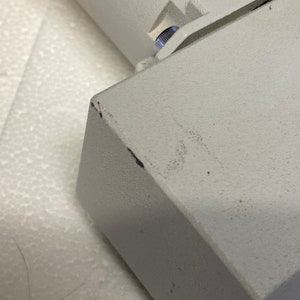 May include: Close-up of a white metal object with a small silver screw. The object has a textured surface and appears to be part of a larger piece of equipment.