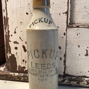 May include: A vintage ceramic bottle with a brown ceramic stopper. The bottle is white with black lettering that reads "PICKUP LEEDS" and "TO BUY, SELL OR USE THIS BOTTLE IS ILLEGAL".