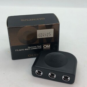 May include: Black Olympus TTL Auto Multi Connector for electronic flash. The connector has three ports and the text "TTL Auto" is printed on the top.