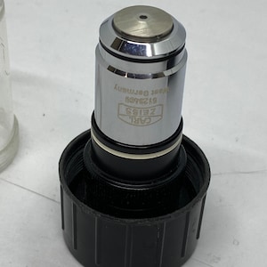 May include: A silver microscope objective lens with the text "CARL ZEISS" and "612349" and "W. GERMANY" engraved on the side.