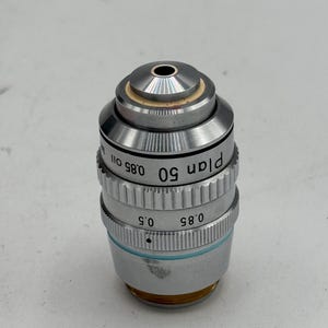 May include: A silver microscope objective lens with the text "plan 50 0.85 011" printed on the side.