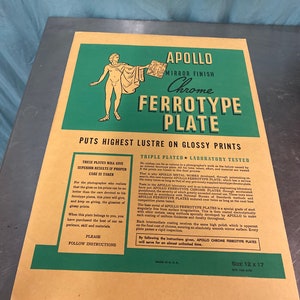 May include: A green and gold poster advertising Apollo Chrome Ferrotype Plates. The poster features a drawing of a nude figure holding a plate. The text on the poster reads "Apollo Chrome Ferrotype Plate, Puts Highest Lustre on Glossy Prints, Triple Plated Laboratory Tested, Size 12 x 17".