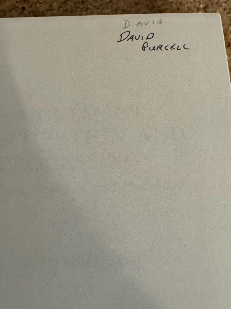 May include: A light gray paper with handwritten text. The text reads "David Purcell" with the word "David" in a larger font size. Above the name is the word "David" in a smaller font size.